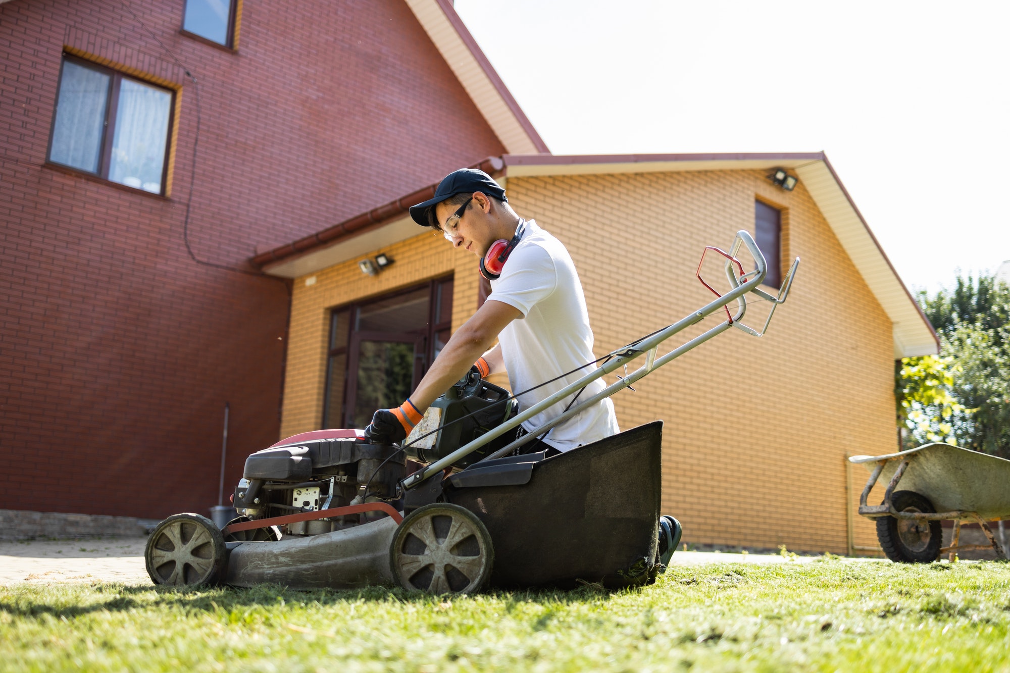 Man with a can of gasoline in his hands unscrews the fuel cap of a lawn mower